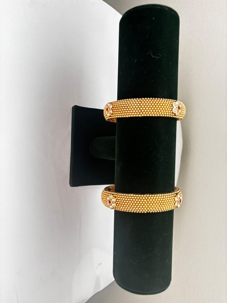 Pair of antique gold beaded bangles with ruby red and white floral motifs on black velvet bangle stand